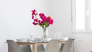Una mesa de comedor con cuatro sillas, un florero con flores y dos copas de vino.