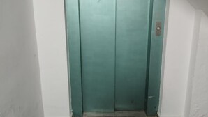 Puerta verde de ascensor con un picaporte de metal y un pequeño panel de control a la derecha.