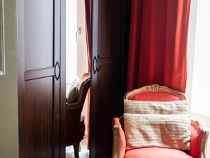 Ein Zimmer mit einem Holzschrank, einem roten Sessel mit weißem Kissen und einem roten Vorhang.