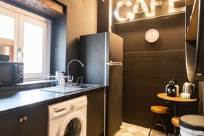 Eine kompakte Küche mit Waschmaschine, einer Kaffeemaschine und einem kleinen Barhocker.