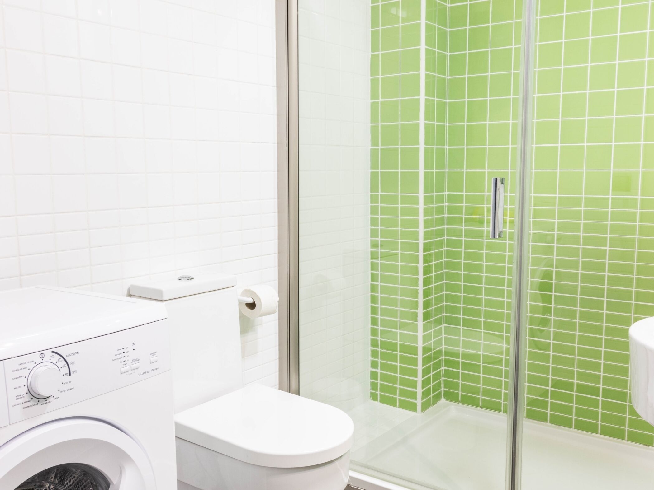 Un baño con lavadora, inodoro y ducha con azulejos verdes.