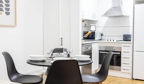 A modern kitchen with white cabinets, a microwave, a stove, and a dining area with a round table and black chairs. - Rincon del Mar - FREE PARKING by Cadiz Time (Ciudad de Cádiz)
