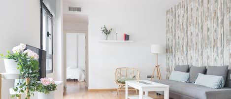 A modern living room with a grey sofa, a white coffee table, a wicker chair, and a floor lamp.