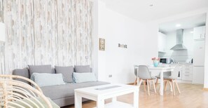 A modern living area with a sofa, a dining table, and a kitchen in the background. - Apartamento Caleta - FREE PARKING by Cadiz Time (Ciudad de Cádiz)