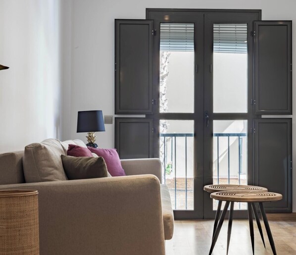 Ein Wohnzimmer mit einer Couch, Kissen, einer Lampe, einem kleinen runden Tisch und einer Glasschiebetür, die auf einen Balkon führt.