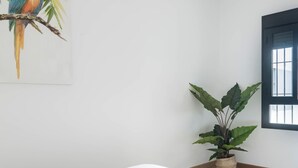 Et minimalistisk hotelværelse med en seng, hvide håndklæder, en potteplante og et billede af en fugl på væggen.