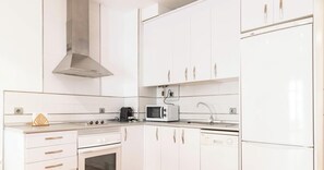 Eine moderne Küche mit weißen Schränken, einer Edelstahl-Dunstabzugshaube, einer Mikrowelle, einer Kaffeemaschine und einem Kühlschrank.