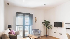 En stue med sofa, stol, fjernsyn, en plante og en dør til en balkon.