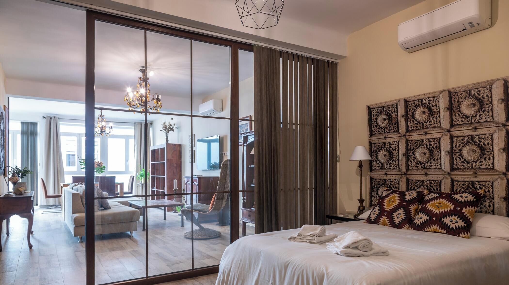 Ein Hotelzimmer mit einem Bett, einem großen Spiegel, einer Chandelüster und einer Wand mit dekorativen Paneelen.