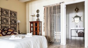 Ein Hotelzimmer mit Bett, einem Holzschrank, einer Wand mit Dekoration, einer Perlenvorhang und einem Badezimmer mit Spiegel und Waschbecken.