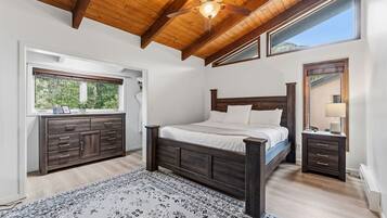 Ein Schlafzimmer mit Holzboden, einem großen Bett, einem Nachttisch, einer Kommode und einem Fenster mit Blick auf Grünflächen.