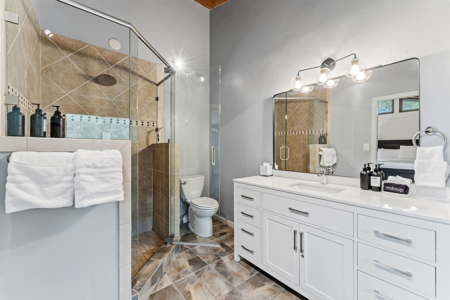 A modern bathroom with a glass shower enclosure, a white vanity with a large mirror, and a toilet.