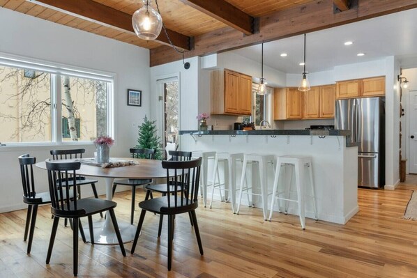 Eine moderne Küche mit Holzschränken, einem Edelstahlkühlschrank und einer Bar mit weißen Hocker.