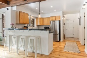 Eine moderne Küche mit Holzschränken, einem Edelstahlkühlschrank und weißen Barhocker.