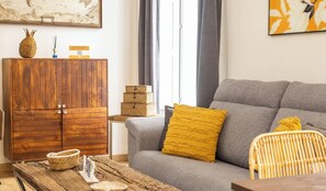 Ein Wohnzimmer mit grauem Sofa, einem Holzkabinett, Korbwannen und einem Tisch mit Dekoration.