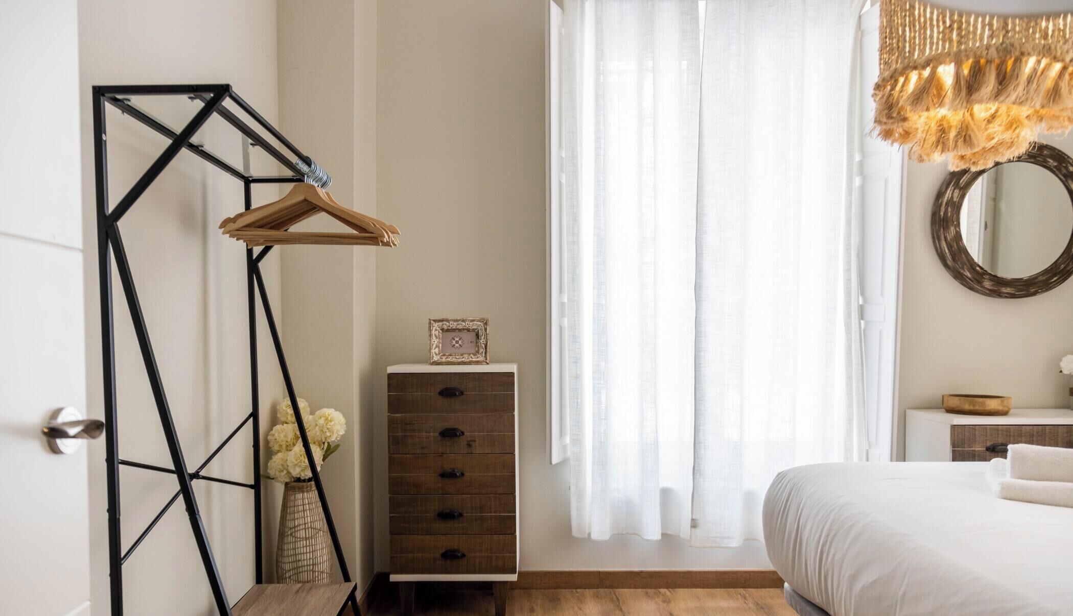 Un dormitorio con cama, cómoda, espejo y lámpara colgante.
