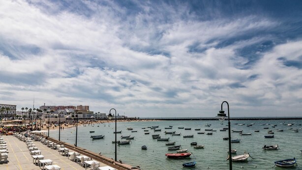 A coastal scene with a beach, boats, and a promenade with tables and chairs. - Tailor's Home by Cadiz Time (Ciudad de Cádiz)