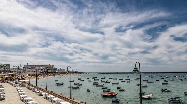 A coastal scene with a beach, boats, and a promenade with tables and chairs. - Tailor's Home by Cadiz Time (Ciudad de Cádiz)