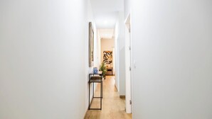A narrow hallway with a wooden floor, white walls, and a door at the end leading to a room with a large abstract painting. - Tailor's Home by Cadiz Time (Ciudad de Cádiz)