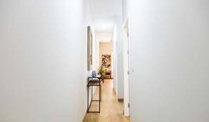 A narrow hallway with a wooden floor, white walls, and a door at the end leading to a room with a large abstract painting. - Tailor's Home by Cadiz Time (Ciudad de Cádiz)