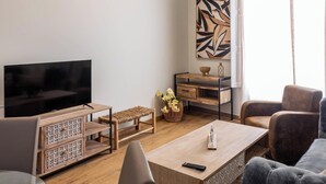 A living room with a TV, a wooden coffee table, a bench, a chair, and a desk with a vase of flowers. - Tailor's Home by Cadiz Time (Ciudad de Cádiz)