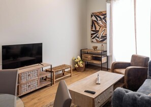 A living room with a TV, a wooden coffee table, a bench, a chair, and a desk with a vase of flowers. - Tailor's Home by Cadiz Time (Ciudad de Cádiz)