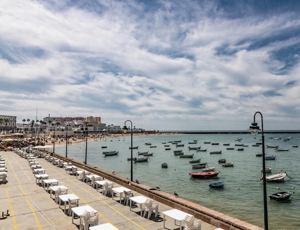 A coastal scene with a beach, boats, and a promenade with tables and chairs. - Casa Rehala PAYA by Cadiz Time (Ciudad de Cádiz)