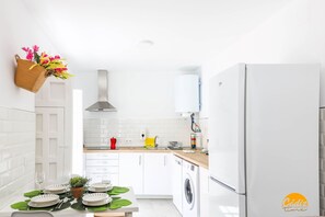 A modern kitchen with white cabinets, a washing machine, and a dining area set with plates and glasses. - Casa Rehala PAYA by Cadiz Time (Ciudad de Cádiz)