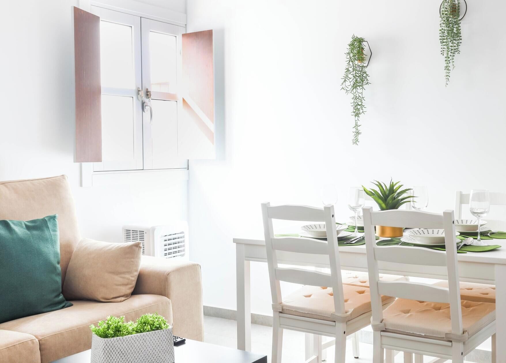 Ein modernes Wohnzimmer mit einer Couch, einem Esstisch für zwei Personen und einer hängenden Pflanze.