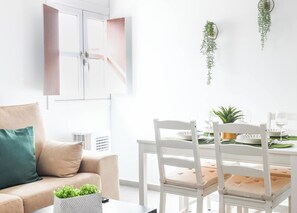 Ein modernes Wohnzimmer mit einer Couch, einem Esstisch für zwei Personen und einer hängenden Pflanze.