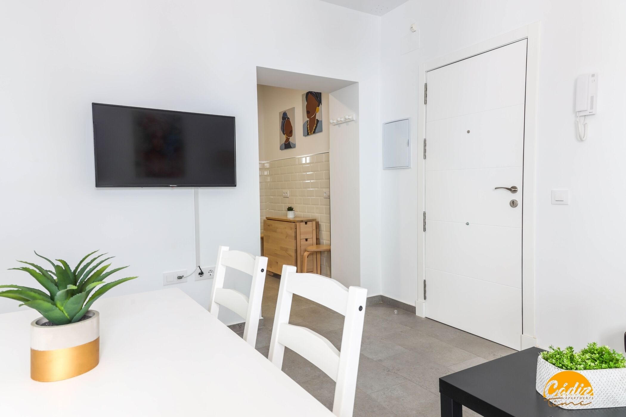 Une cuisine moderne avec un téléviseur, des chaises blanches, une table à manger et une plante en pot.