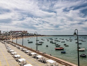 A coastal scene with a beach, boats, and a promenade with tables and chairs. - Casa Rehala YOR by Cadiz Time (Cádiz)