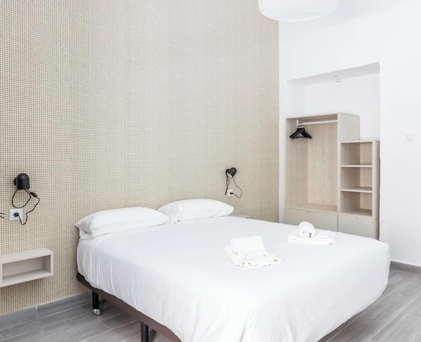 A modern hotel room with a large bed, a wardrobe, a wall-mounted lamp, and a shelf. - The Yellow House by Cadiz Time (Ciudad de Cádiz)