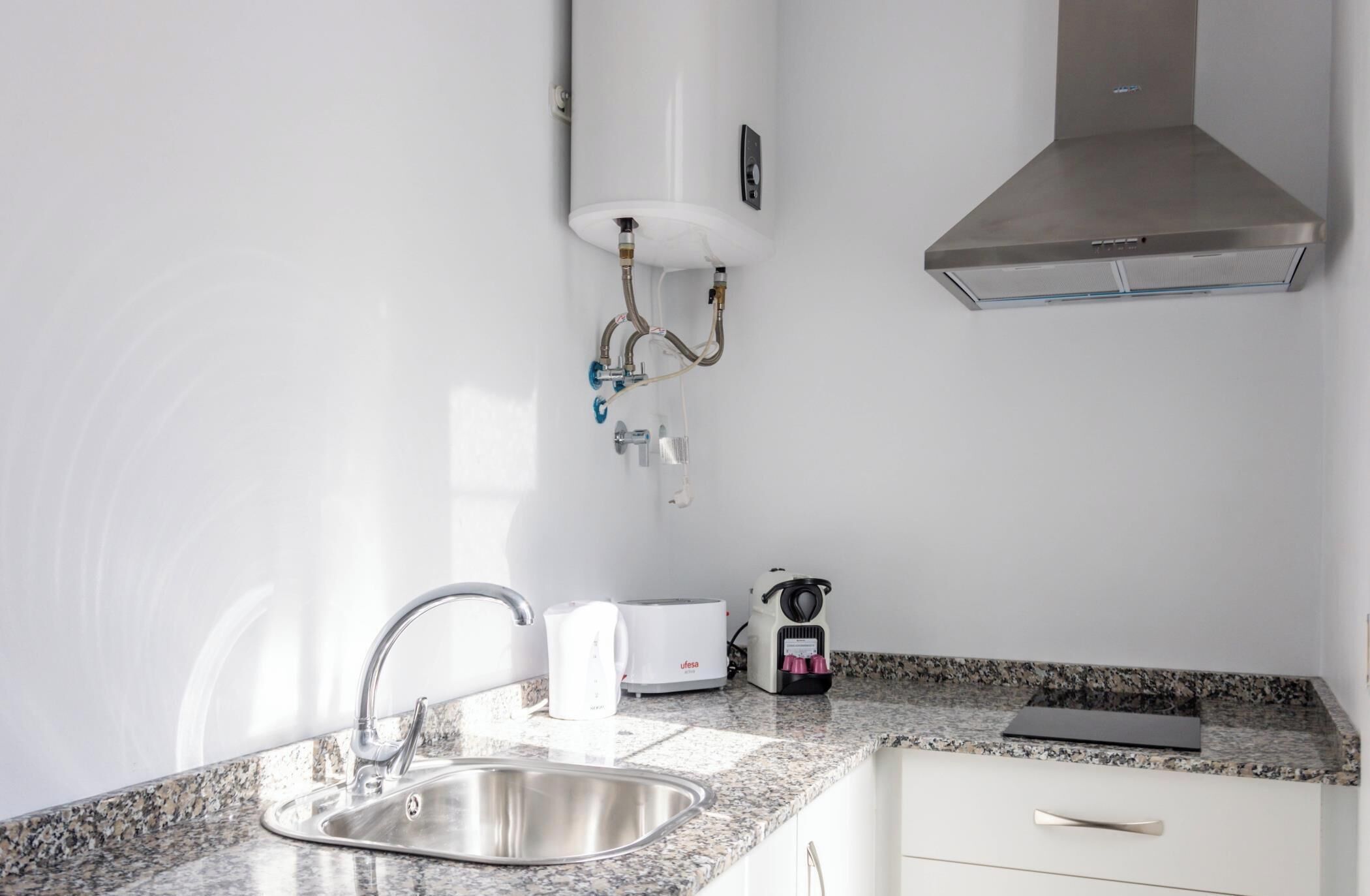 A kitchen with a stainless steel sink, a toaster, a kettle, and a range hood.
