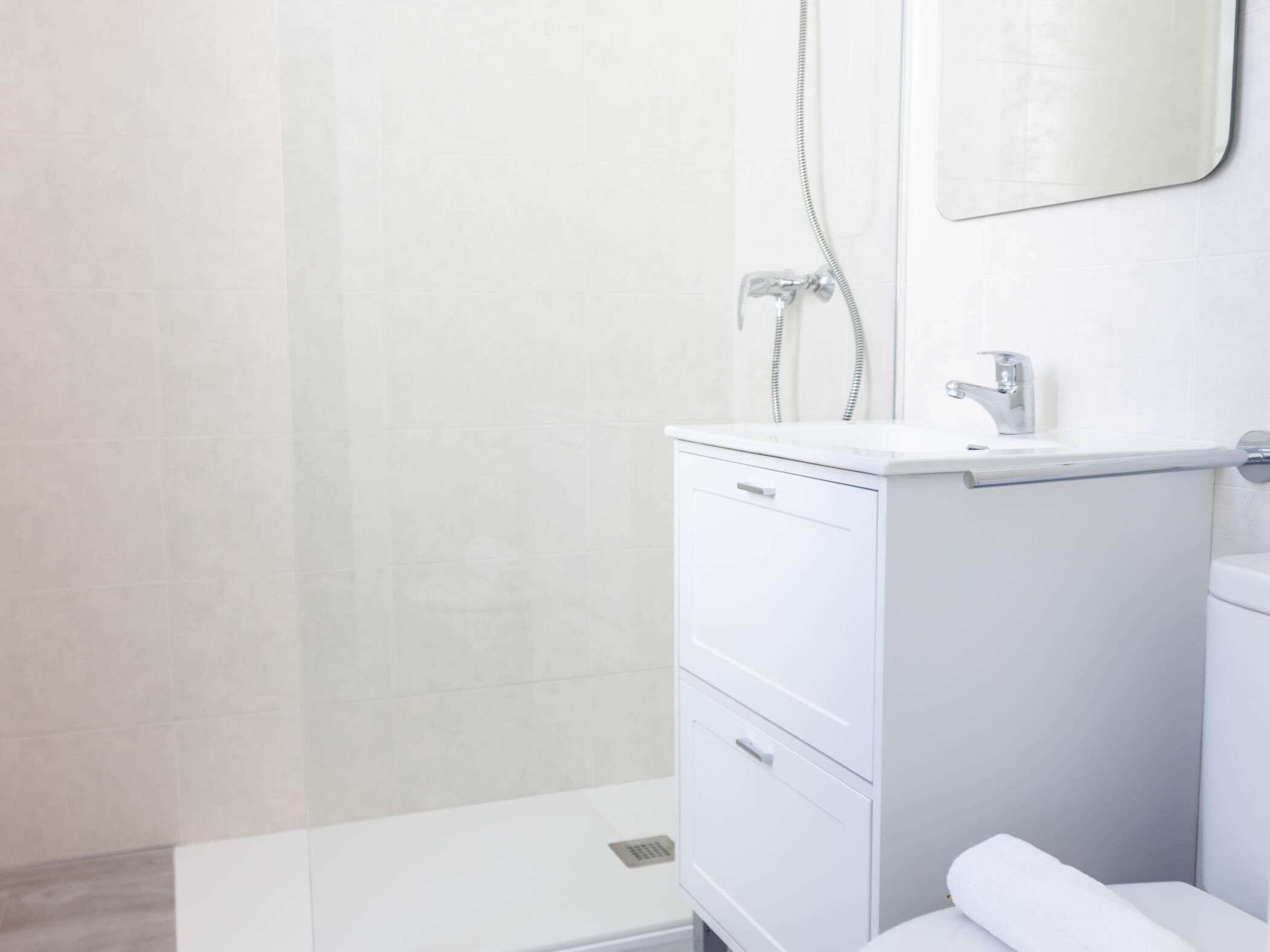 Un baño moderno con un tocador blanco, un espejo y una ducha.
