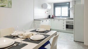 A dining area with a table set for four, a kitchen with white cabinets and appliances, and a window providing natural light. - Loft Santa Maria by Cadiz Time (Ciudad de Cádiz)