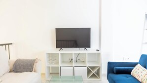 A living room with a flat-screen TV on a white stand, a blue sofa, and a glass coffee table. - Loft Santa Maria by Cadiz Time (Ciudad de Cádiz)