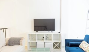 A living room with a flat-screen TV on a white stand, a blue sofa, and a glass coffee table. - Loft Santa Maria by Cadiz Time (Ciudad de Cádiz)