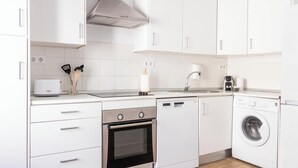 A modern kitchen with white cabinets, a built-in oven, a dishwasher, and a washing machine. - La Luz de La Viña -by Cadiz Time (Ciudad de Cádiz)