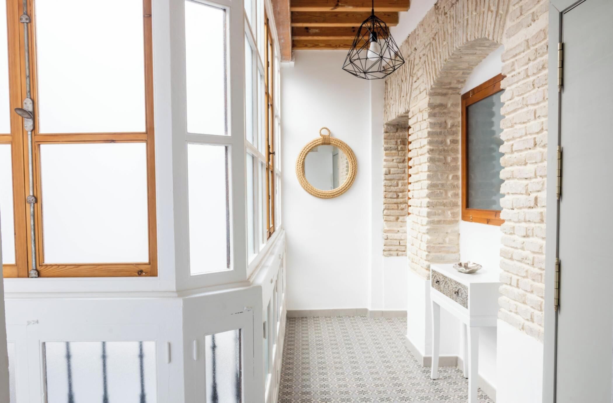 A hallway with a white door, a round mirror, a white console table, and a brick wall.