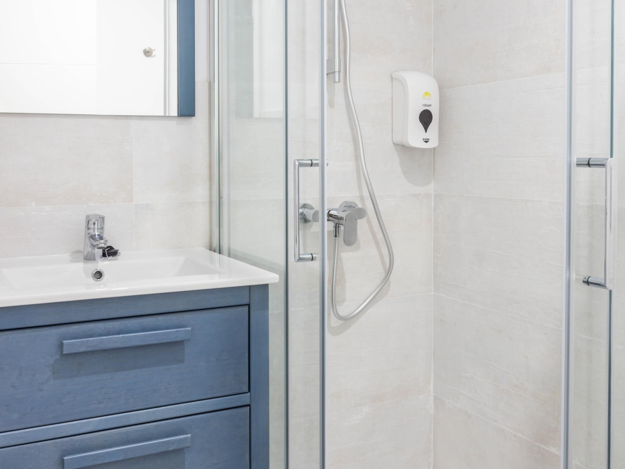 A bathroom with a glass shower enclosure, a white sink, and a soap dispenser.