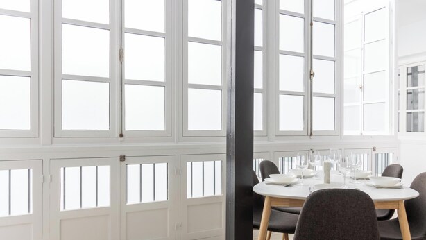 A dining area with a round table set for four, large windows, and a white interior. - Apartamento Bike by LiveWork (Ciudad de Cádiz)