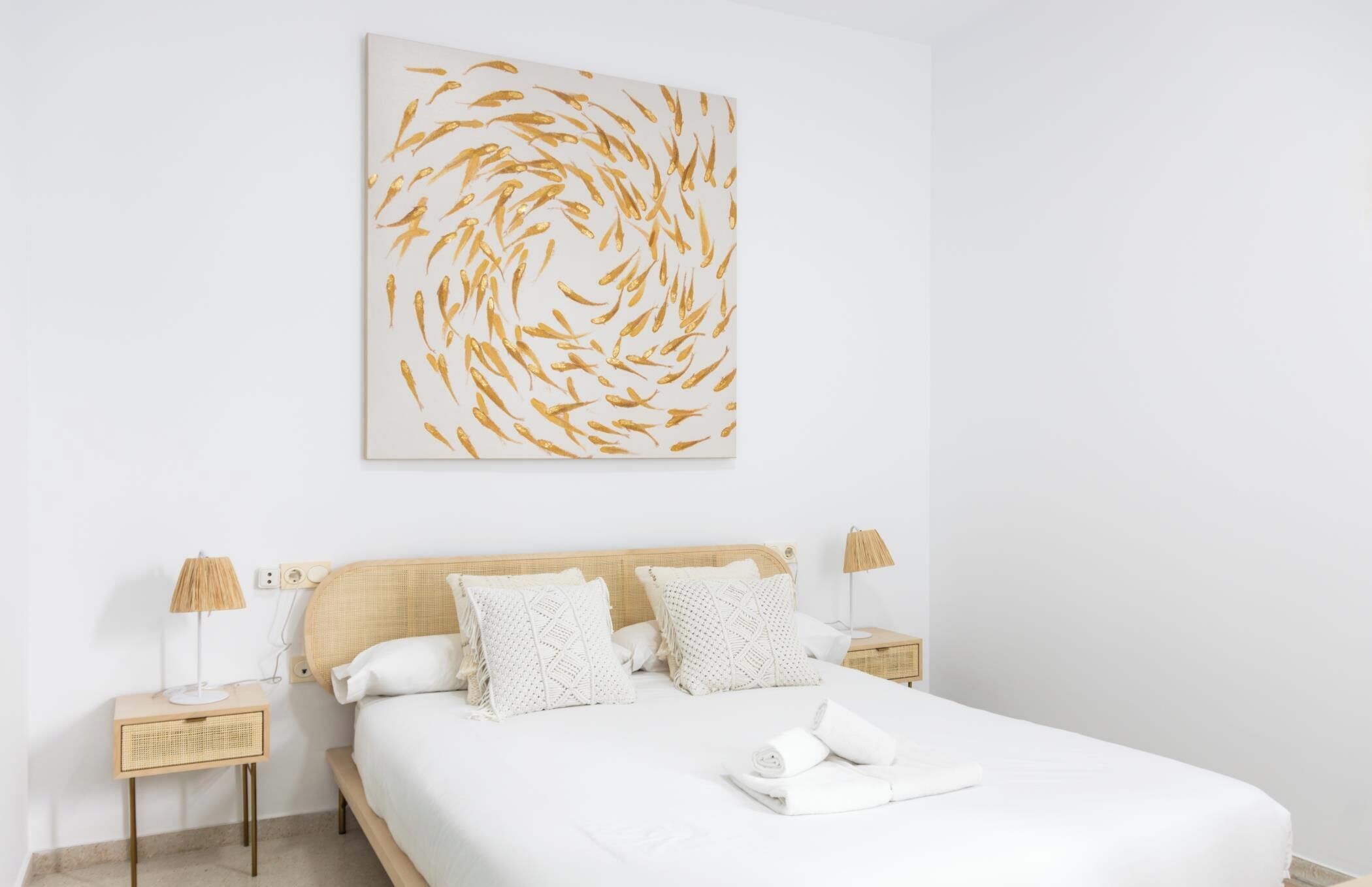 Ein Schlafzimmer mit einem großen Bett, zwei Nachttischen, einem Wandbild und einem ordentlich bezogenen Bett.