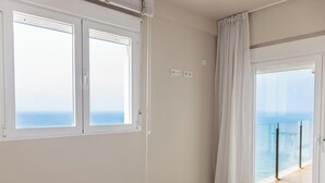 Quarto com cama, janela com vista para o mar e varanda com guarda-corpo de vidro.