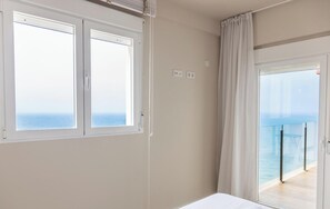 Ein Zimmer mit Bett, einem Fenster mit Meerblick und einem Balkon mit Glasgeländer.
