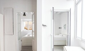 A hallway leading to a bedroom with a bed, a window with curtains, and a door. - Flamenco Centro by Cadiz Time (Ciudad de Cádiz)