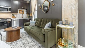 En moderne stue med sofa, rundt sofabord, sofabord med glasplade og et køkken i baggrunden.