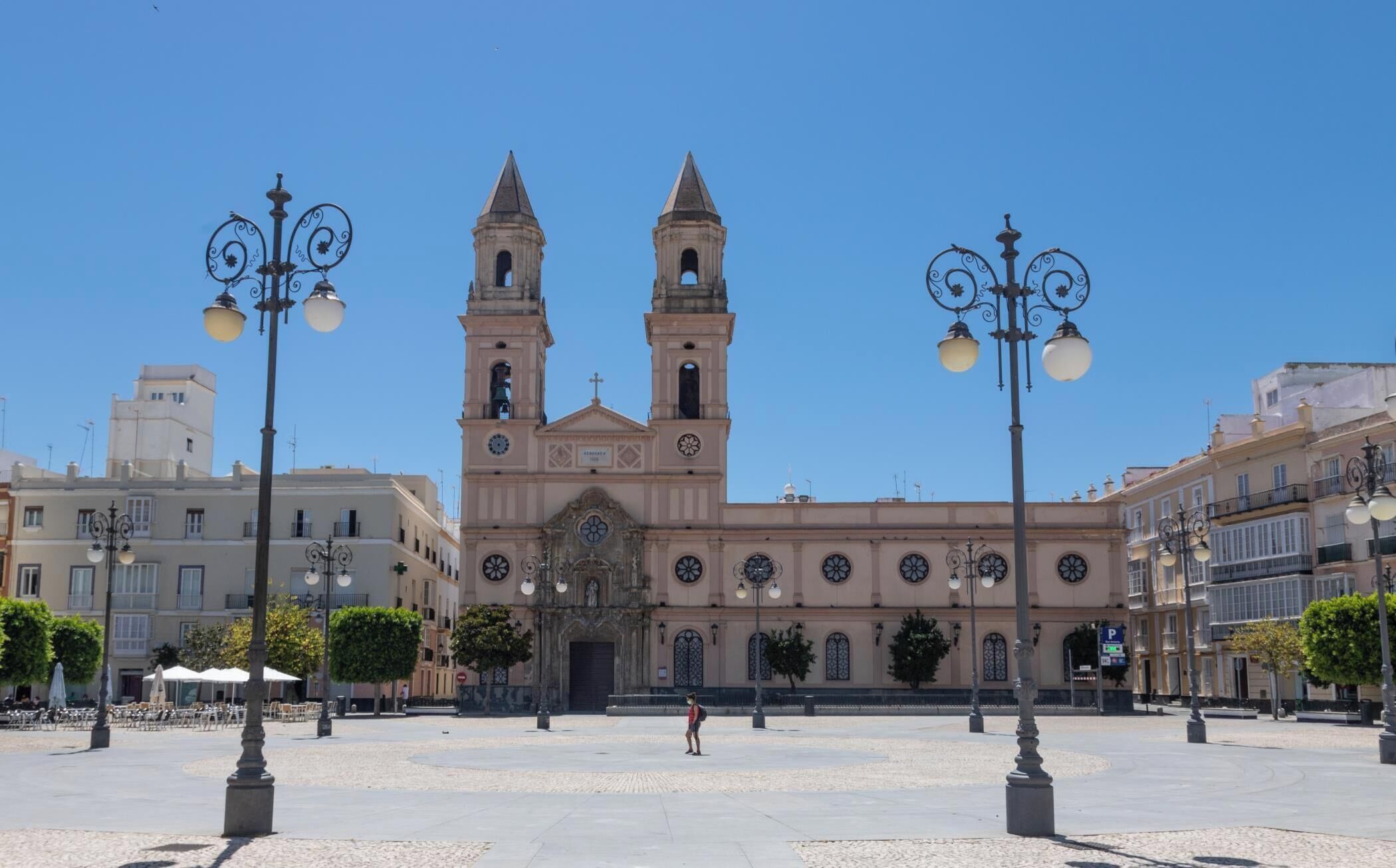 A historic building with two towers, a central entrance, and a paved square with street lamps.