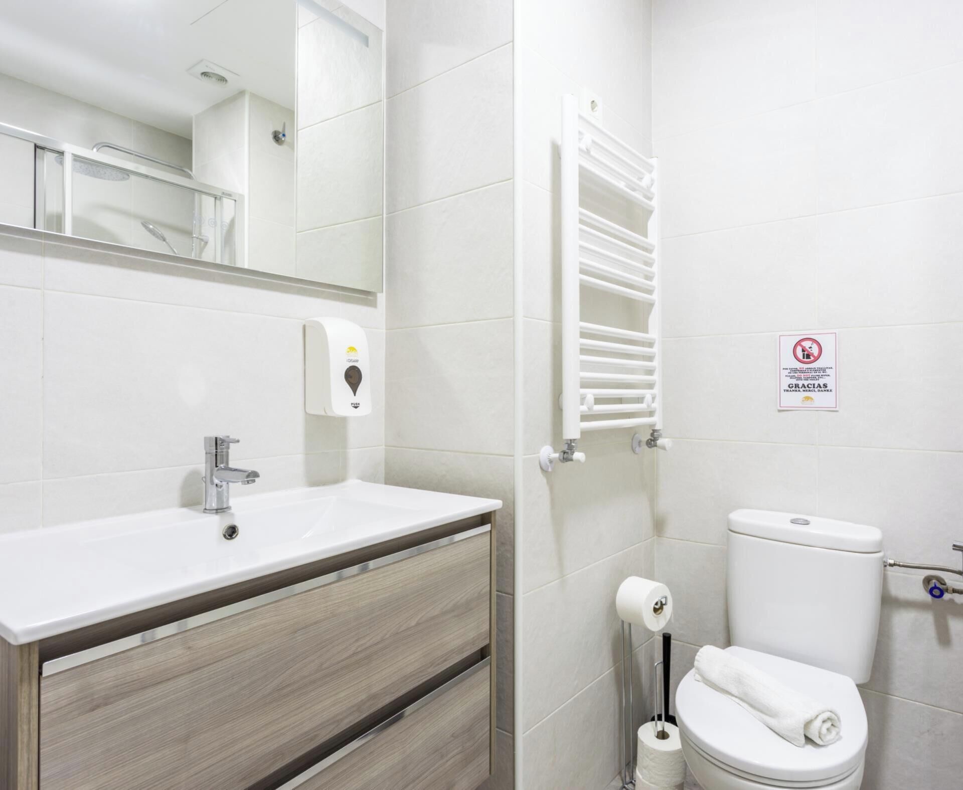 A bathroom with a sink, mirror, towel rack, toilet, and a no-smoking sign.