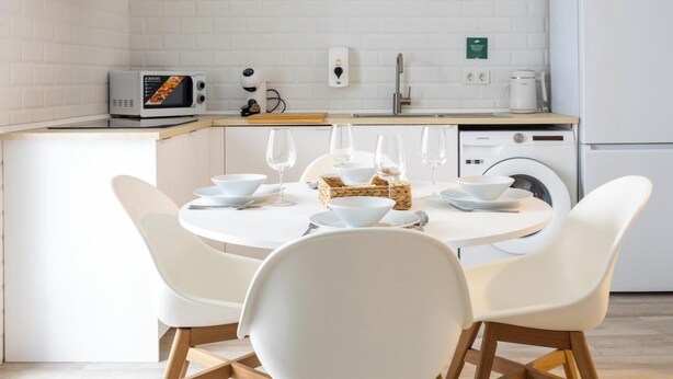 A modern kitchen with white appliances, a dining table with white chairs, and a built-in washing machine. - Bajo Teatro Falla by Cadiz Time (Ciudad de Cádiz)